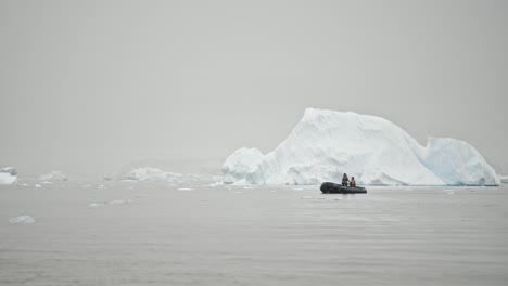 two people in boat cruising around a big ice berg in polar region