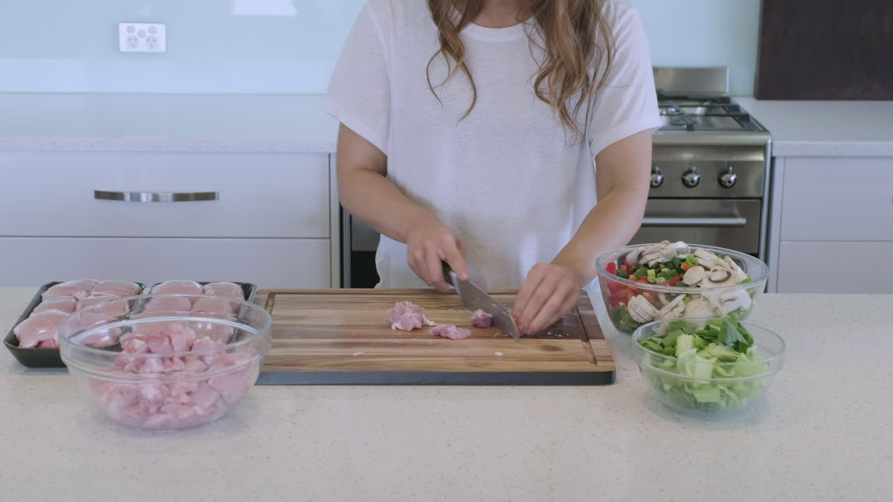 foto frontal de una mujer en la cocina de casa cortando pollo y preparando verduras para la cena asiática salteada