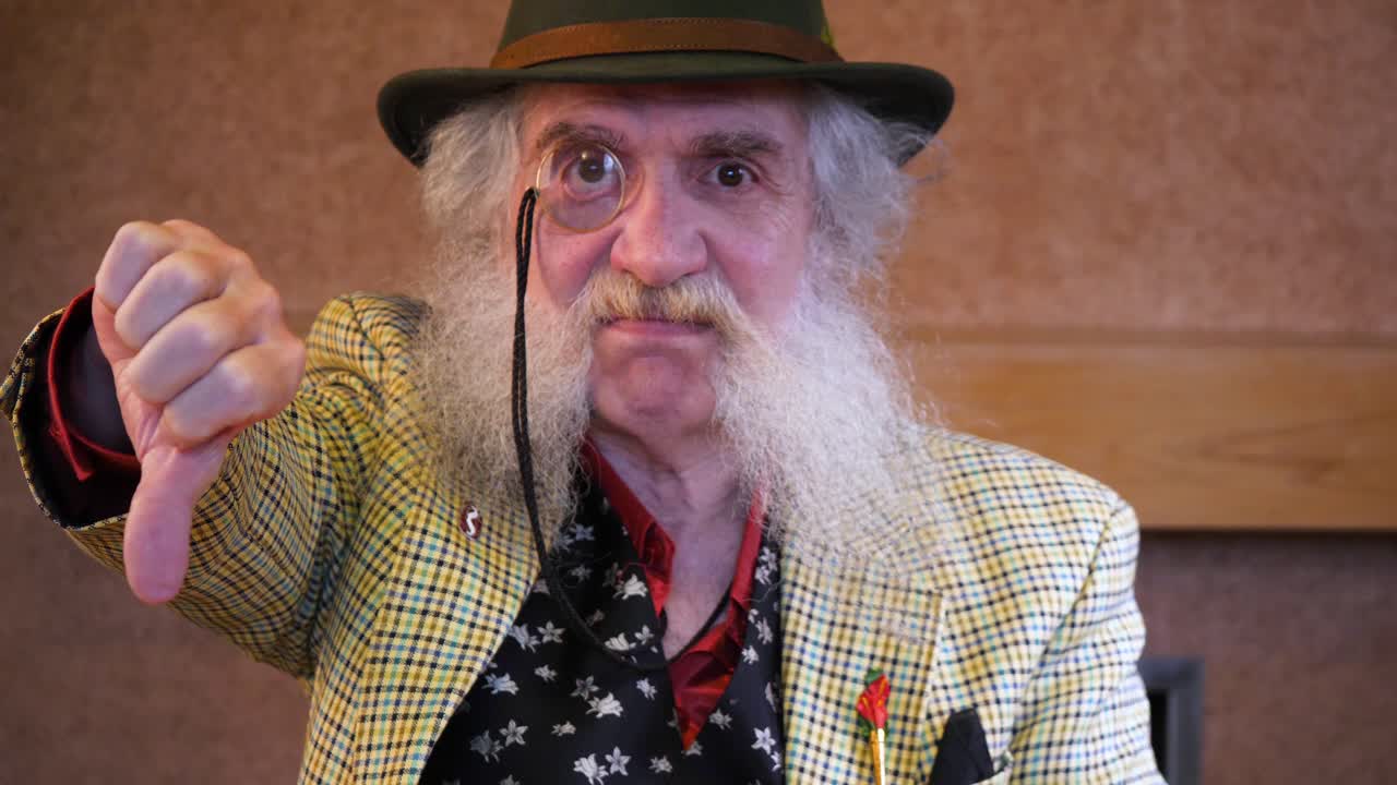 턱수염을 기른 노인이 카메라를 향해 엄지손가락을 내리며