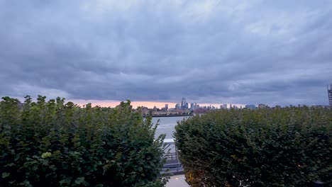 london skyline emerging from river thames under cloudy sky at sunset from westferry circus