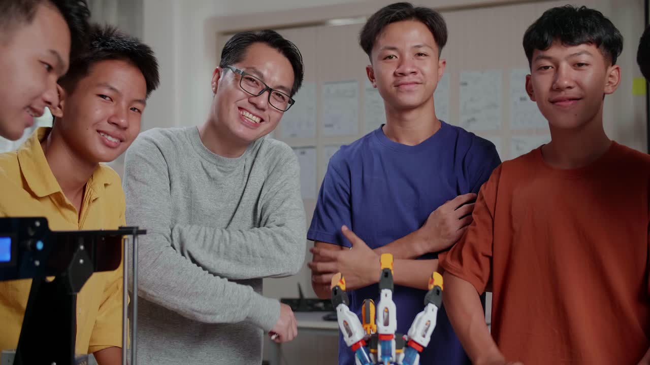 과 3d 프린팅을 가진 아시안 남자와 소년들은 학교에서 사이보그 손에 대해 논의하는 동안 미소 짓고 카메라에 팔을 고 있습니다.