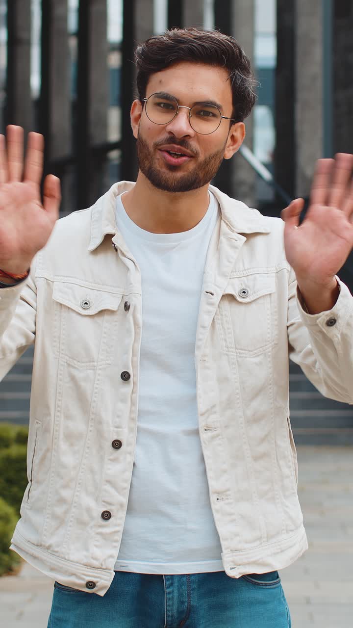 Indian man smiling friendly at camera waving hands hello hi greeting or goodbye in city street