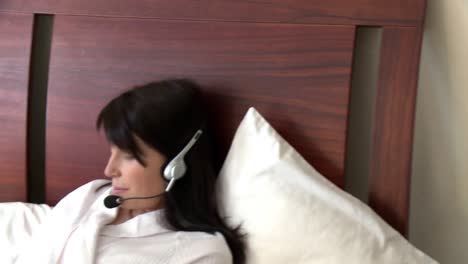 elegant woman with headset on using a laptop sitting on bed