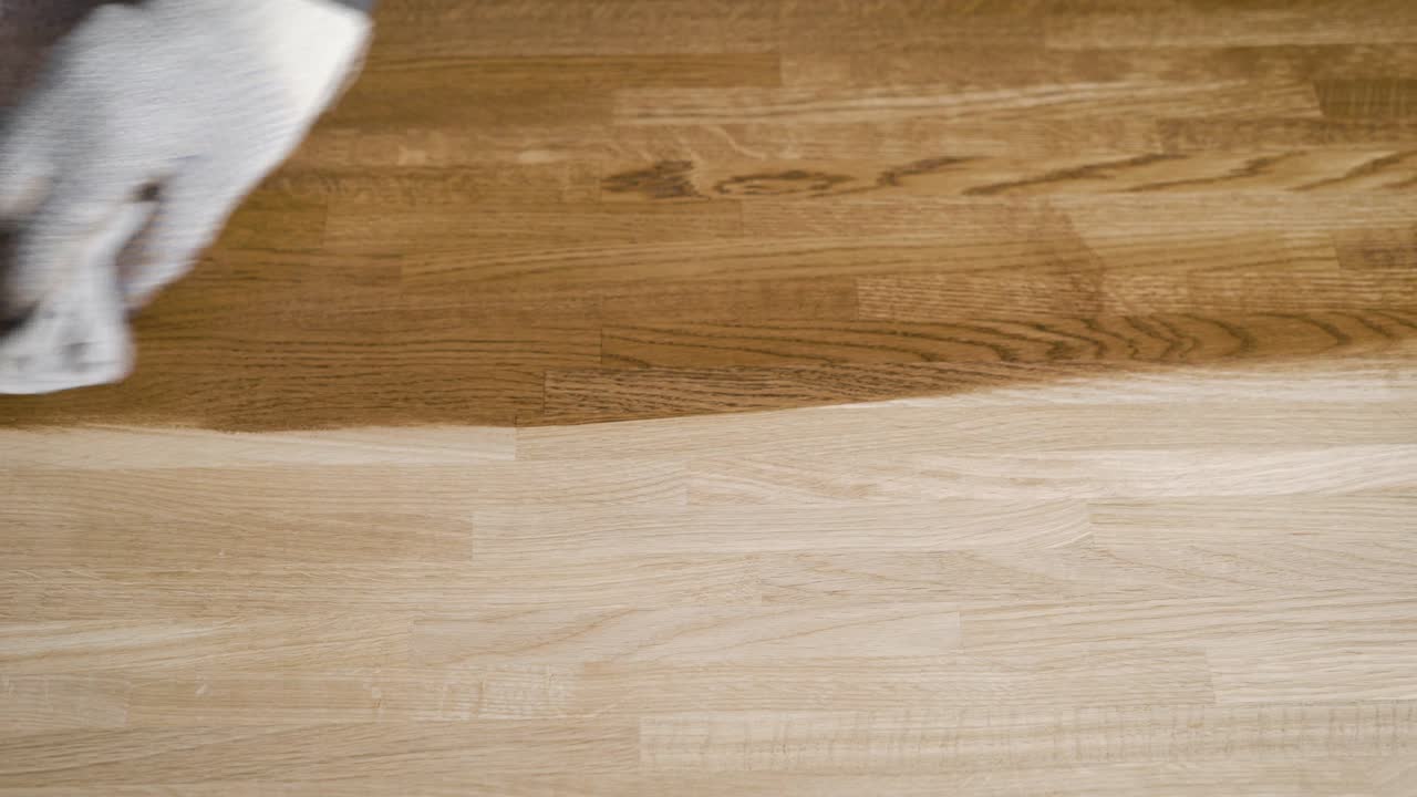 joiner is covering big wooden board by protective composition, using piece of fabric, close-up of hands