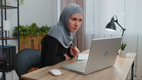 Mujer-De-Negocios-Musulmana-Estudia-Con-Un-Cuaderno-En-La-Oficina-Del-Hogar-En-Una-Computadora-Portátil-Hablando-Con-Una-Cámara-Web-En-Línea