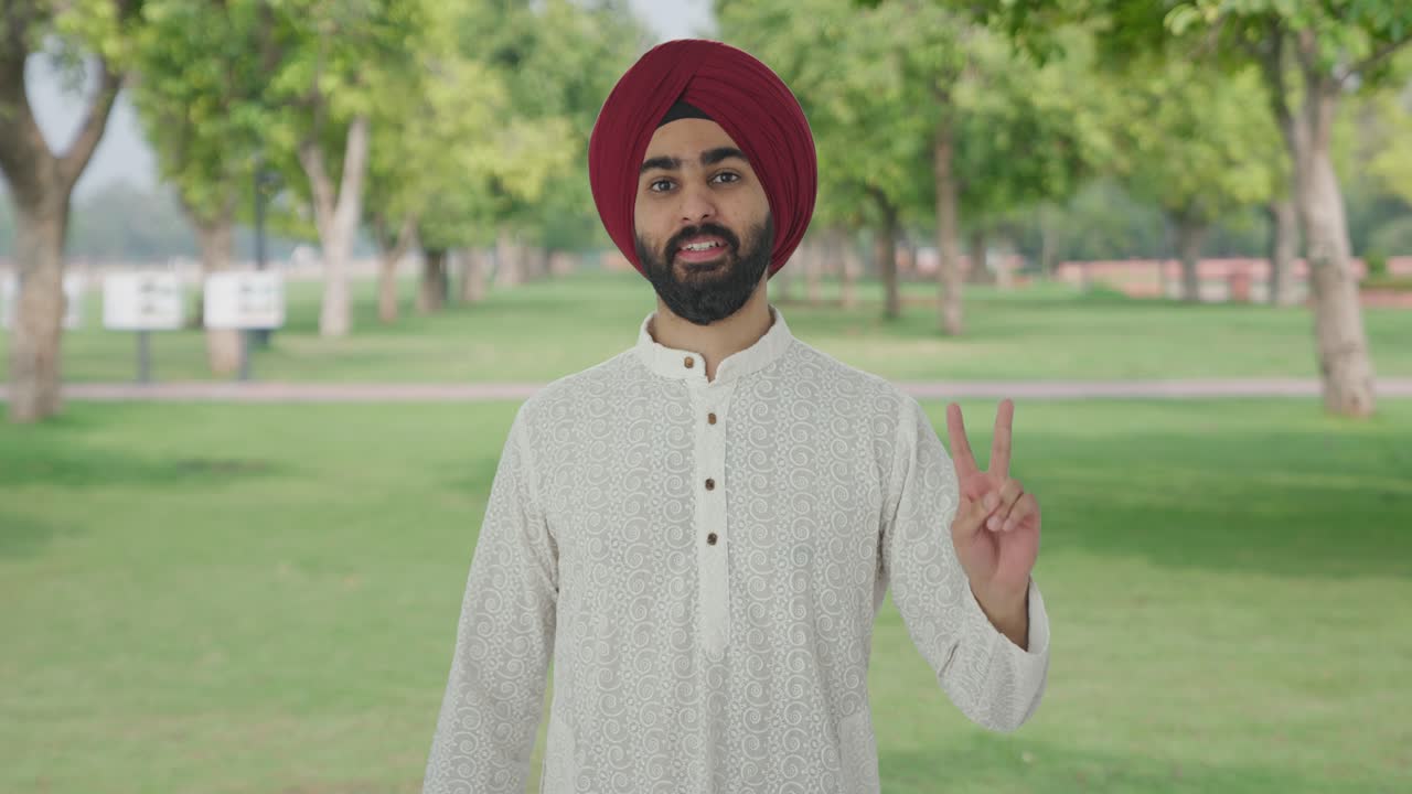 Uomo indiano Sikh che mostra il segno della vittoria nel parco