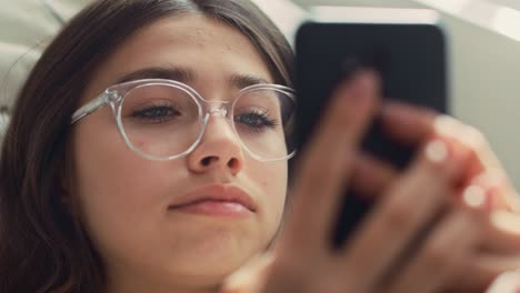 zoom de una adolescente caucásica navegando por el teléfono mientras está acostada en la cama de espaldas