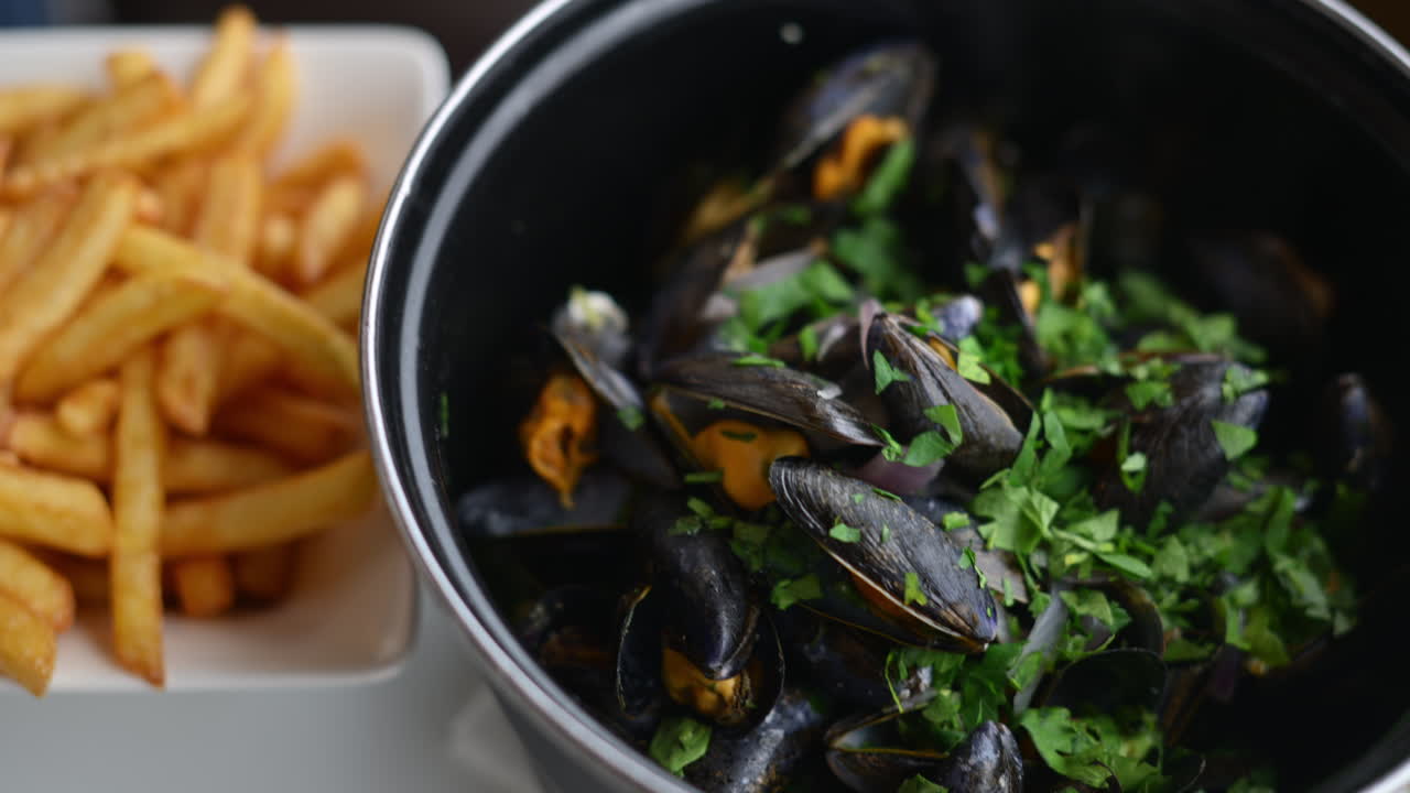 Cooked mussels served in a pot with herbs and sauce, accompanied by golden fries on the side