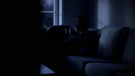 Thoughtful-Man-Sits-Alone-in-Couch-Late-at-Night,-Lit-by-Moonlight,-Looking-Out-Through-Window