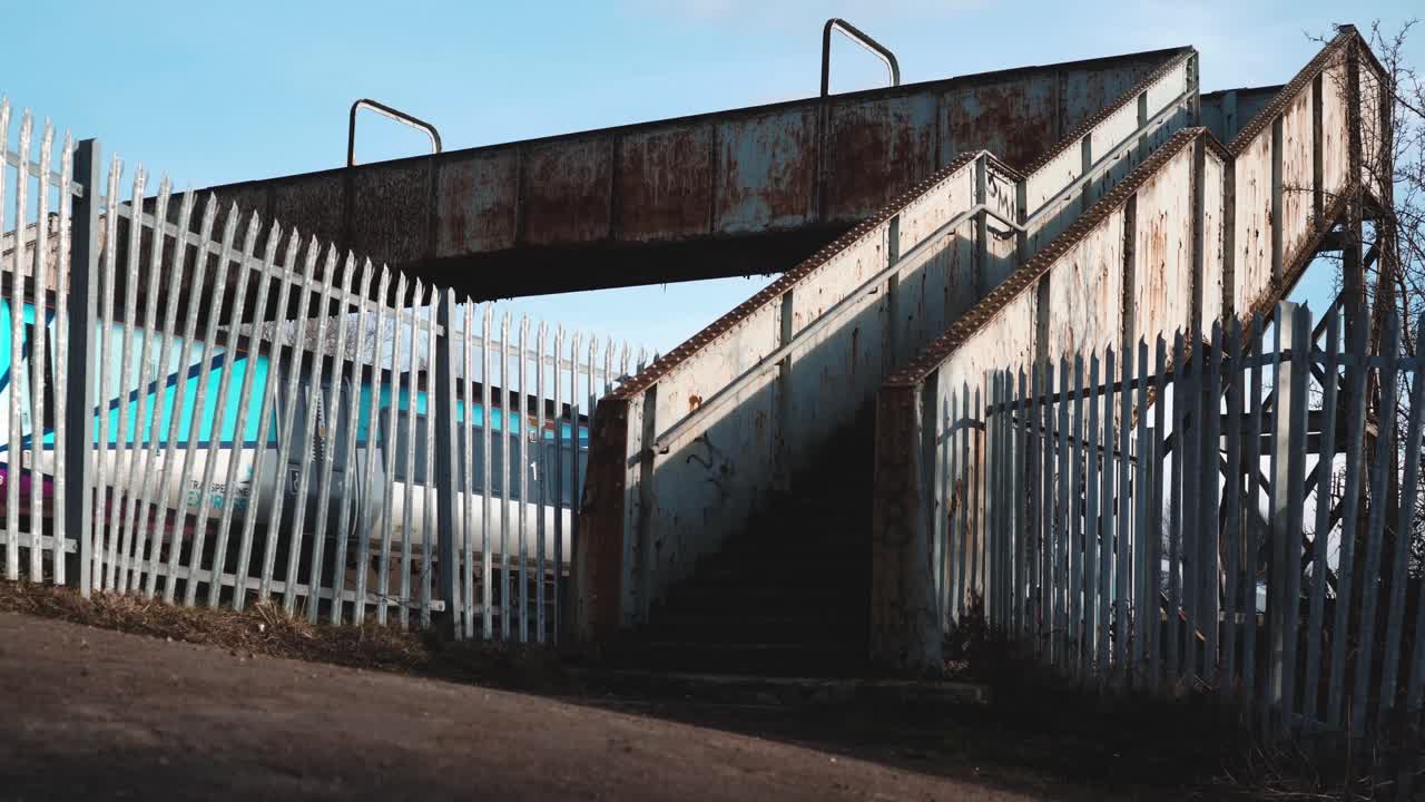 un tren de pasajeros de un solo vagón que pasa bajo un antiguo puente ferroviario peatonal.