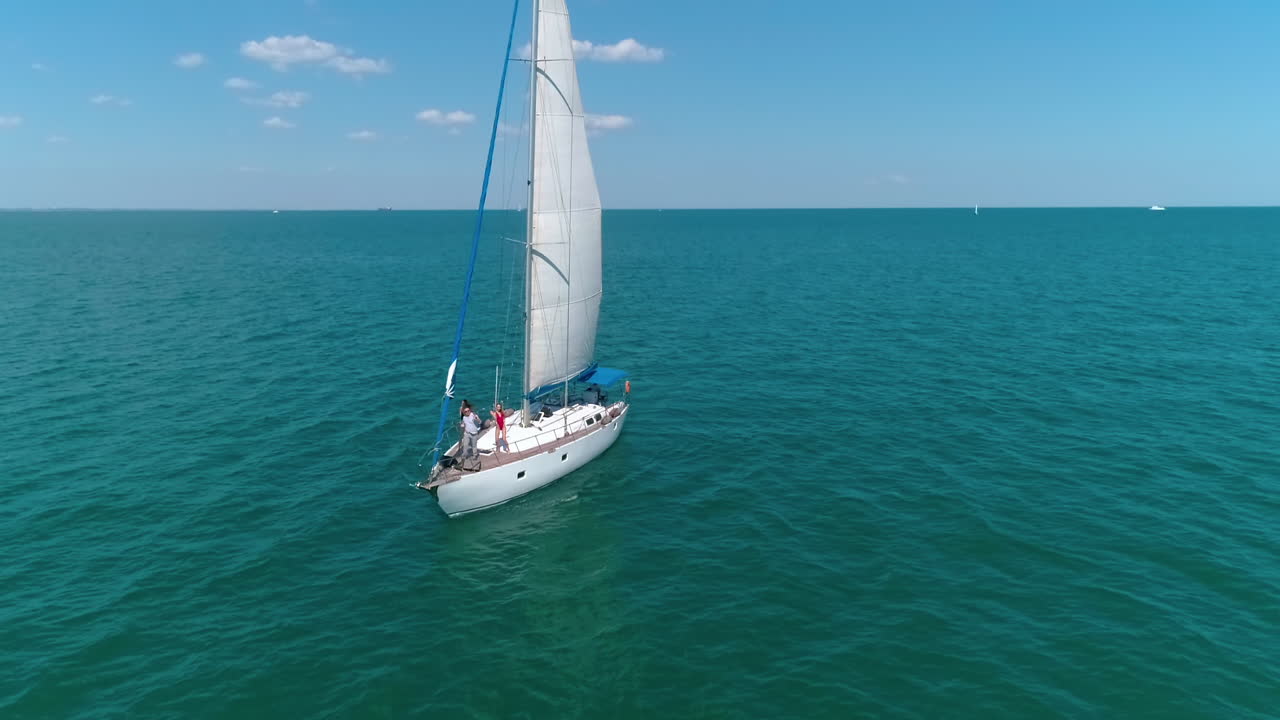 People rest on a sailboat. Voyage on a yacht in the open sea. Girls dancing on a ship while floating on water. Happy summer vacation. Aerial view.