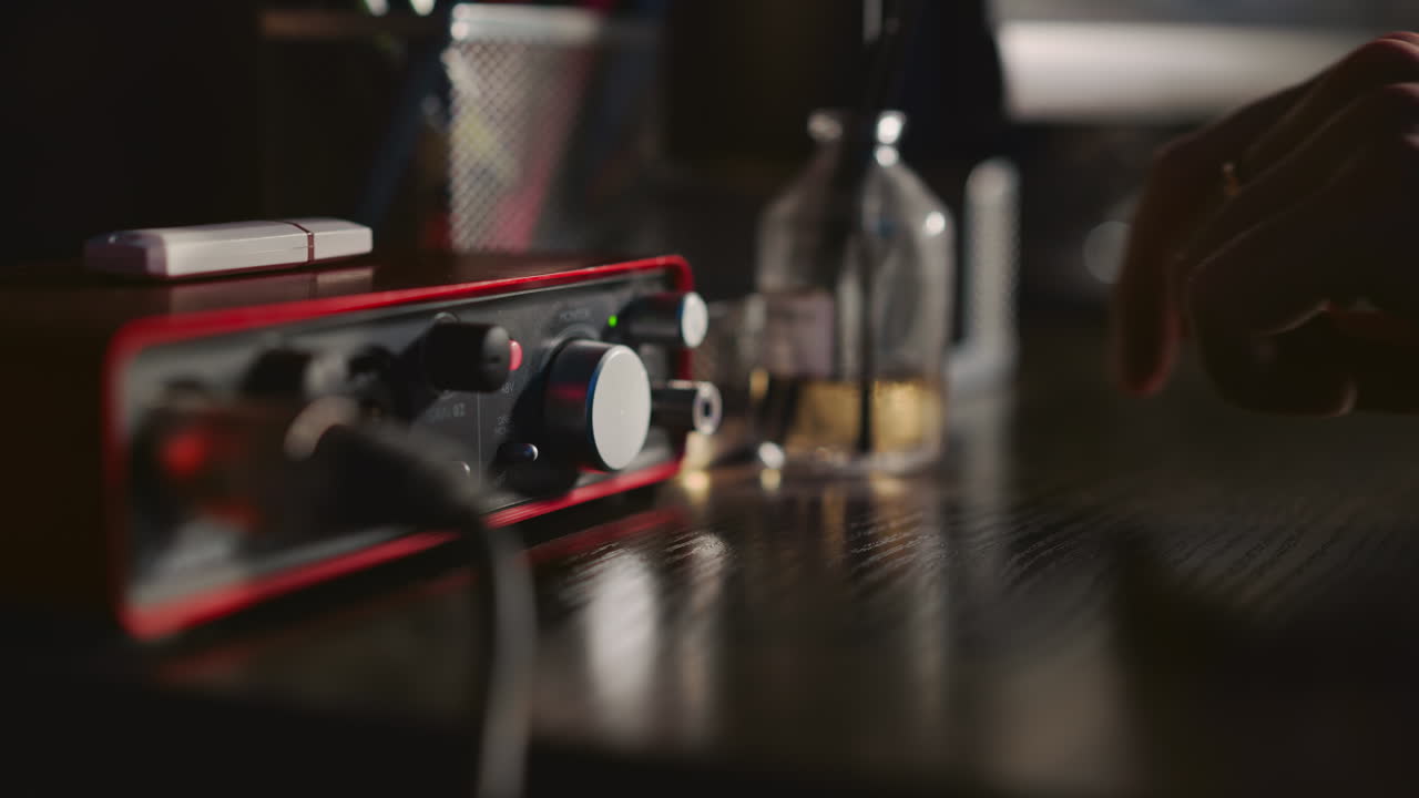 남자가 스튜디오 클로즈업에서 사운드 증폭기를 켜고 음악가가 녹음 스튜디오에서 연주하기 위해 디지털 장비를 준비합니다.