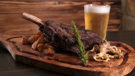 Köstlicher-Knochen-Im-Streifensteak,-Gebratene-Kartoffeln,-Wilde-Waldohrpilze-Und-Rosmarin-Elegant-Angerichtet-Auf-Einem-Holzschneidebrett-Mit-Einem-Frostigen-Bier,-Schieber-Hd