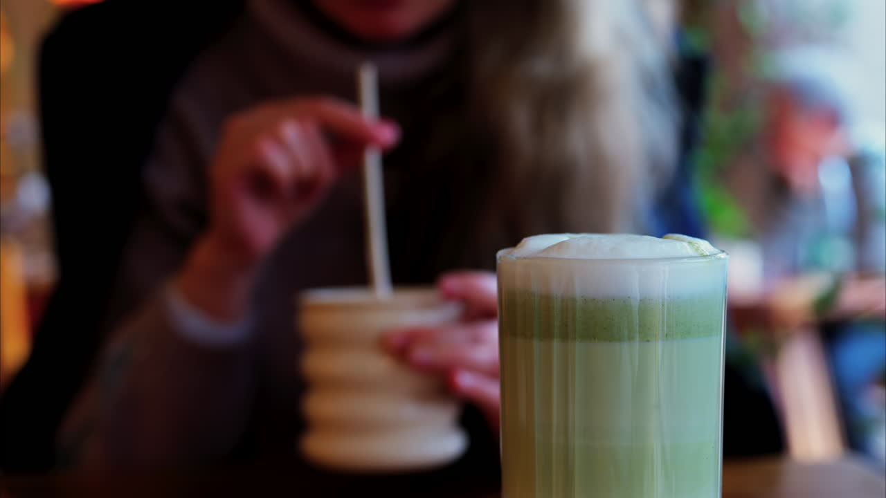 Close up of a matcha latte with a woman drinking at a table at a cafe on the background