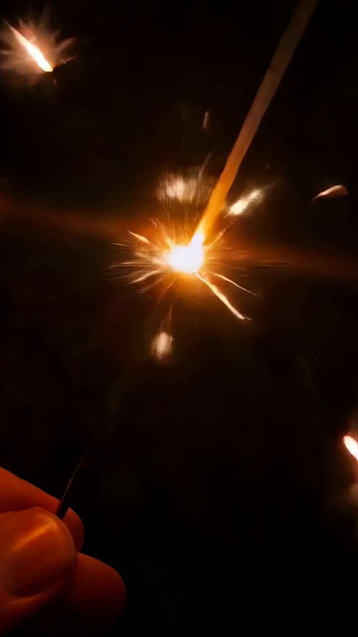 Vídeo vertical: Primer plano de una bengala que emite chispas brillantes en la oscuridad, con un palo cruzado
