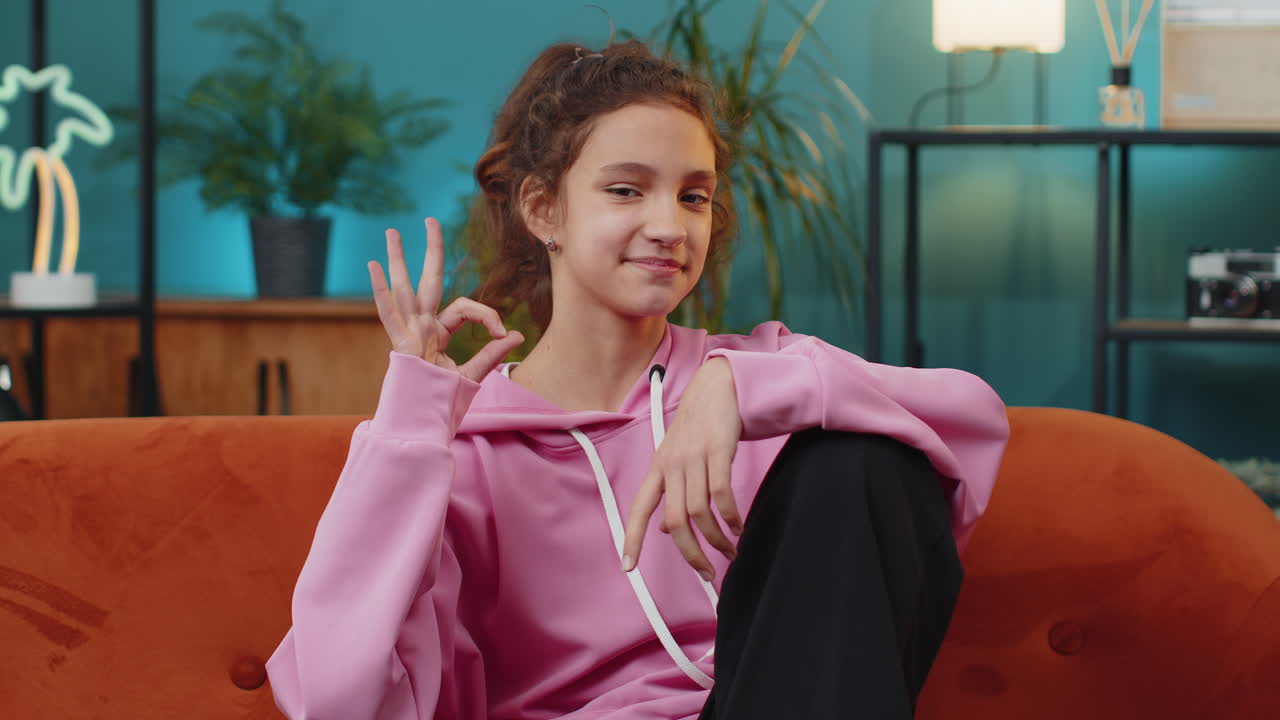 Happy cheerful school girl looking approvingly at camera showing ok gesture positive like sign