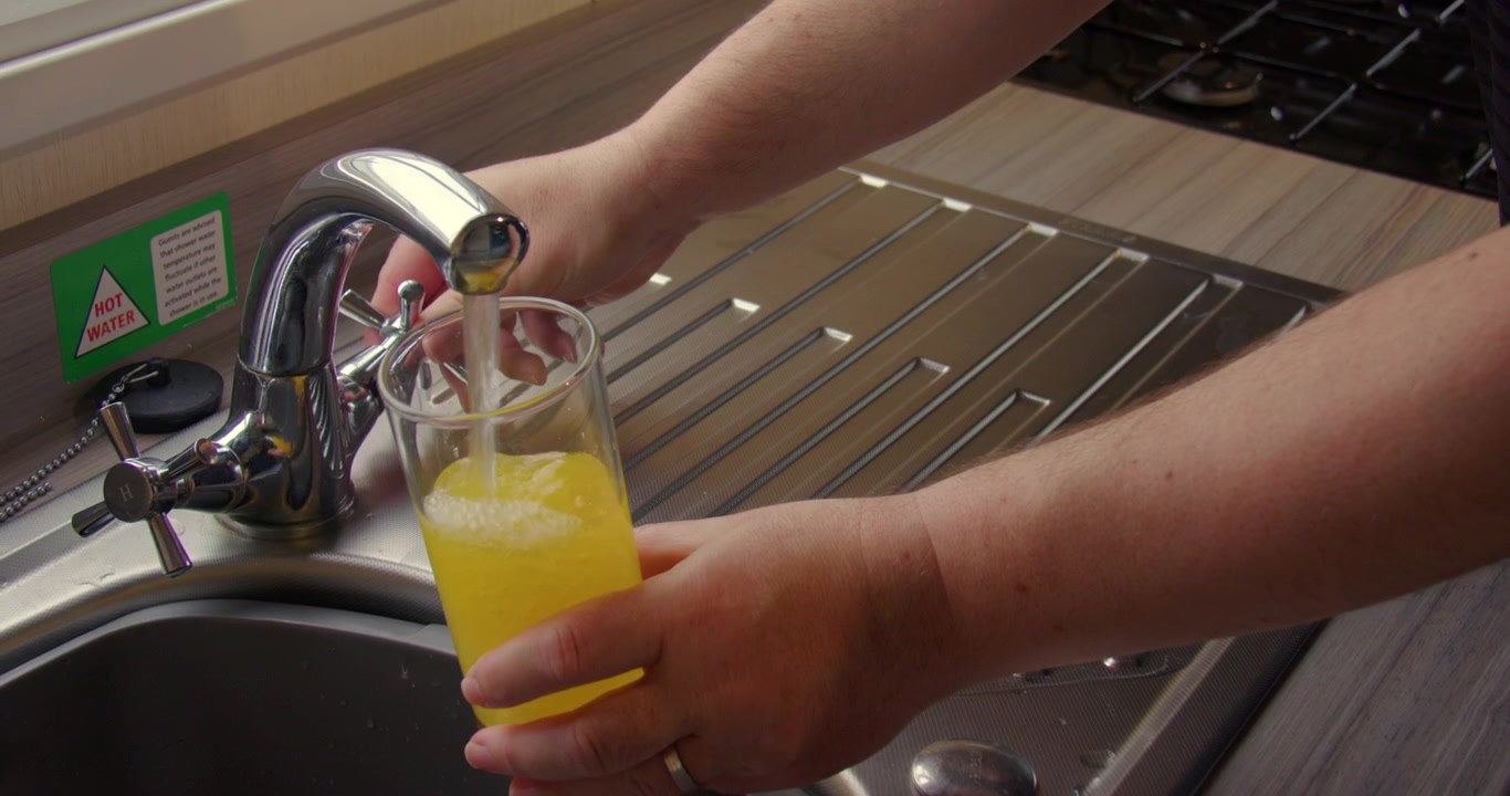 Zoom Shot of orange squash cordial being made in a glass on the kitchen sink.