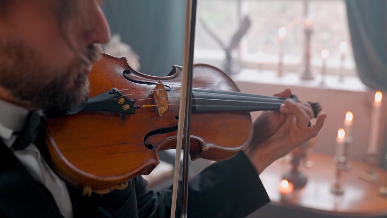 Primo piano di un uomo che suona il violino in una stanza a lume di candela