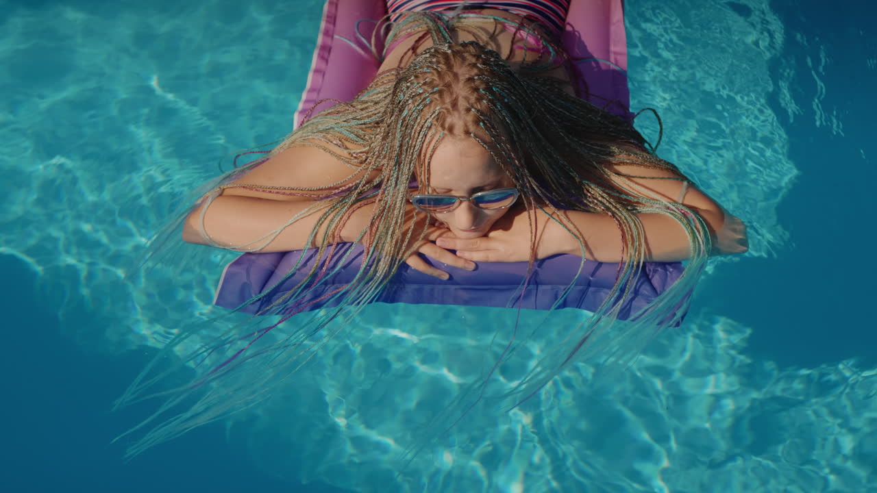 Top view: A child with afro pigtails swims on an inflatable mattress in the pool, resting and enjoying the rest.