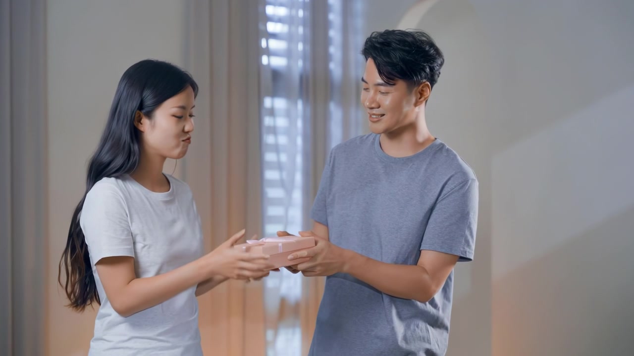 คู่รักสุดโรแมนติกกำลังฉลองโอกาสพิเศษที่บ้าน ชายหนุ่มผู้เปี่ยมรักมอบกล่องของขวัญที่ห่อไว้อย่างสวยงามให้กับภรรยาหรือแฟนสาวผู้มีความสุขของเขา อารมณ์ความรู้สึกที่เต็มไปด้วยความทรงจำ ความสัมพันธ์ การเฉลิมฉลอง และโอกาสพิเศษ