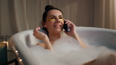 chica de baño llamando por teléfono móvil colocando agua de espuma en casa. señora sonriente hablando