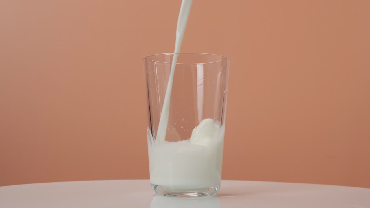 Milk pouring into transparent glass on orange background
