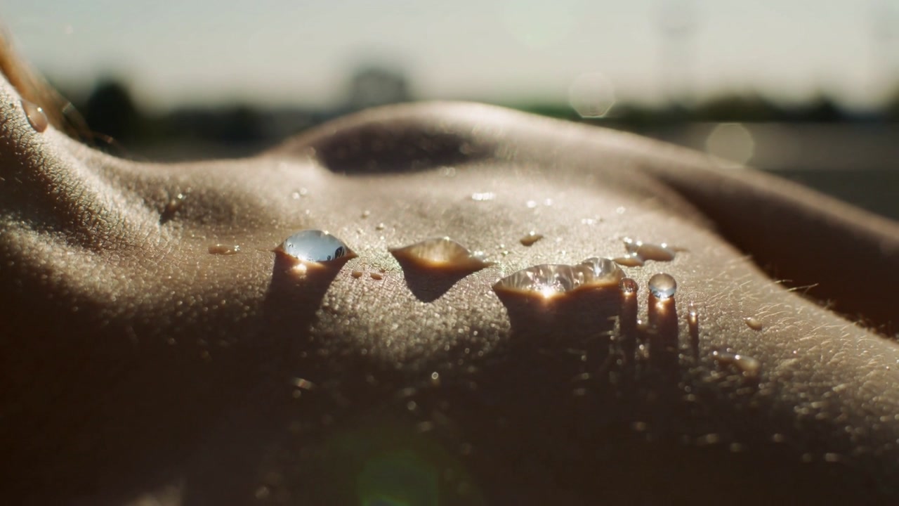 Heating low sun warming female torso skin on sunlit lounger, causing water droplets to elongate