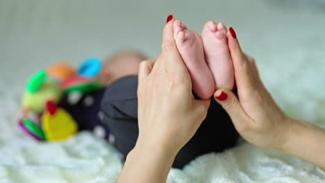 caring mother's hands do a massage to little baby feet. mommy claps and rubs tiny limbs. close up. blurred backdrop.
