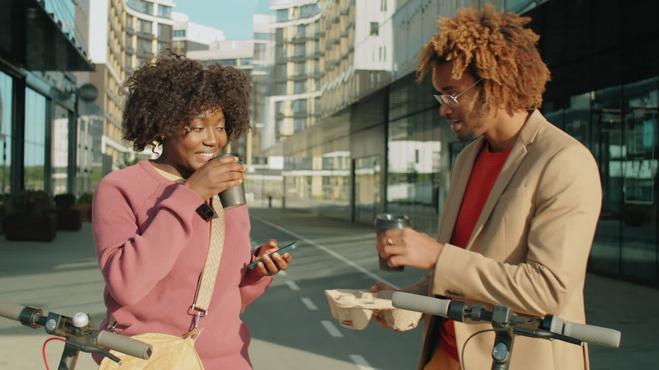 amigos afroamericanos con scooters eléctricos bebiendo café y hablando en la ciudad