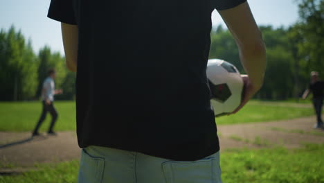 a close-up view of a man rotating a soccer ball around him, with a blurred background showing other people and a child walking by