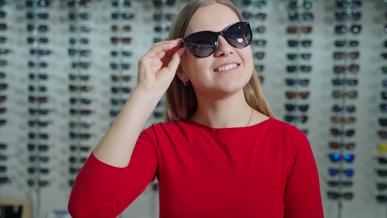 Pretty girl buying new sunglasses. Beautiful smiling young woman tries on stylish glasses and admires herself in the optical store. Summer look.