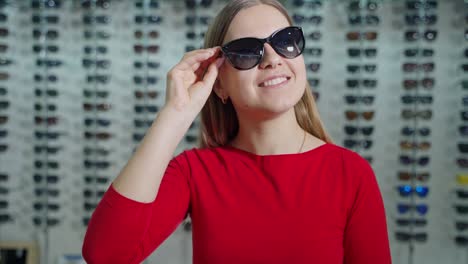 pretty girl buying new sunglasses. beautiful smiling young woman tries on stylish glasses and admires herself in the optical store. summer look.