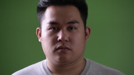 young handsome overweight asian man against green background