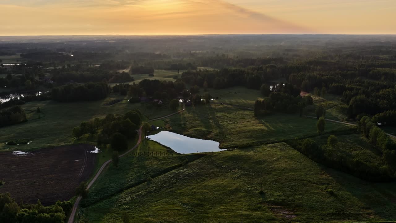 Betagende droneoptagelser, der fanger en fredfyldt solnedgang over frodige grønne marker og en stille sø