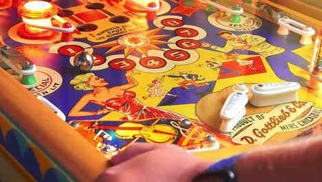 gamer hand play pinball machine with flipper hit ball multiple time, close up handheld fixed shot