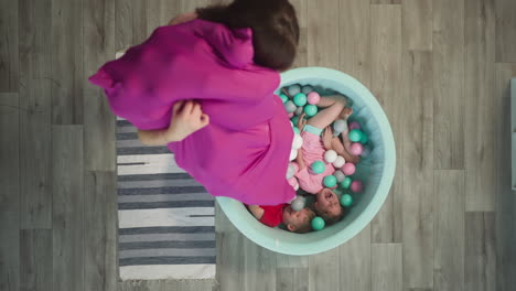 delighted kids lie in dry pool. mother pours out balls