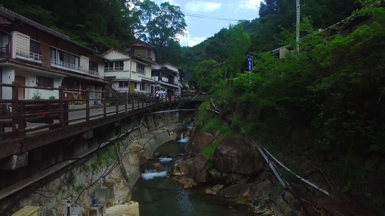 Aerial shot moves ahead, capturing the winding watercourse's path through a charming Japanese village