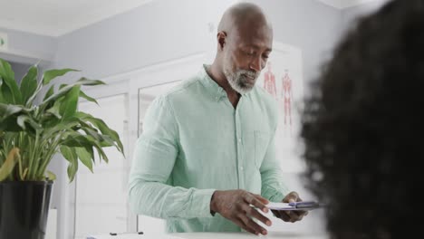 Diverse-medical-receptionist-and-patient-talking-and-signing-documents-at-front-desk,-slow-motion