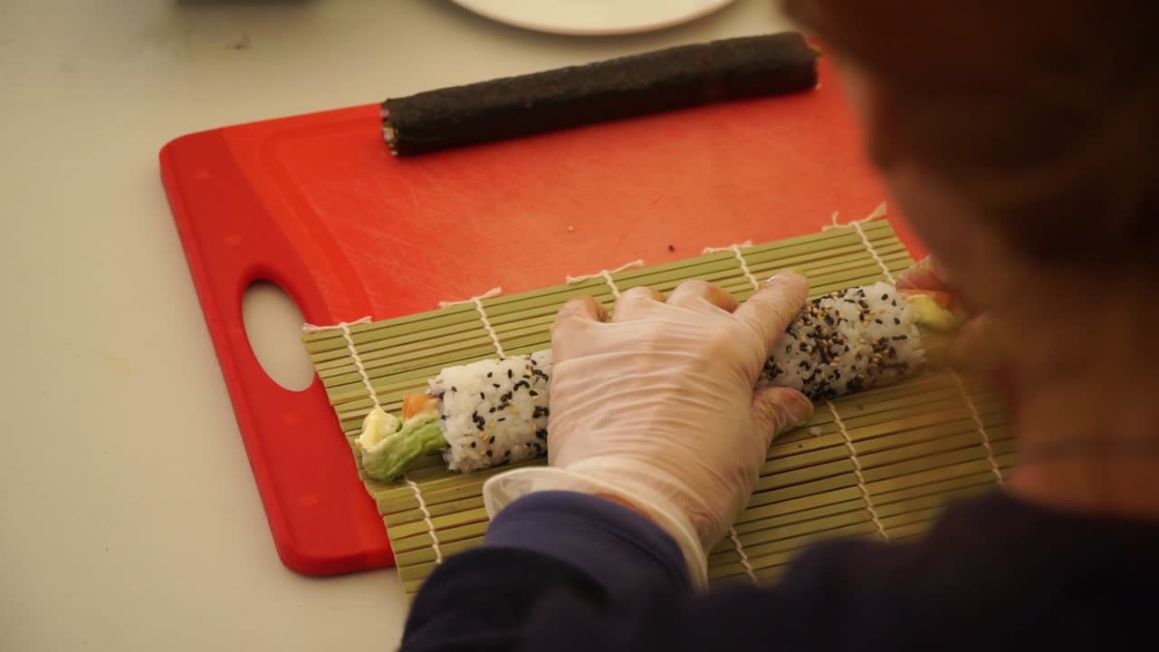 chef japonés preparando rollos de sushi con salmón, aguacate y semillas de sésamo