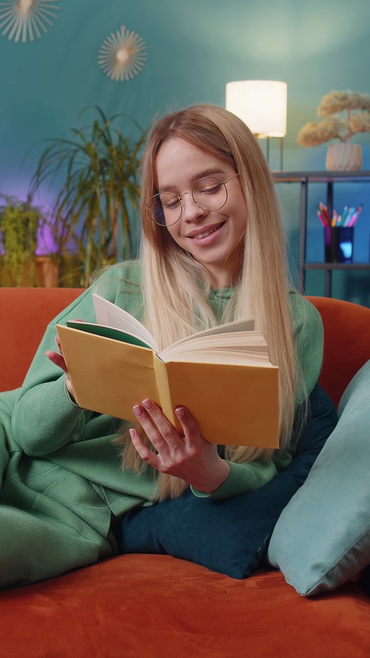 Young woman relaxing interesting book turning pages smiling enjoying literature taking rest on sofa