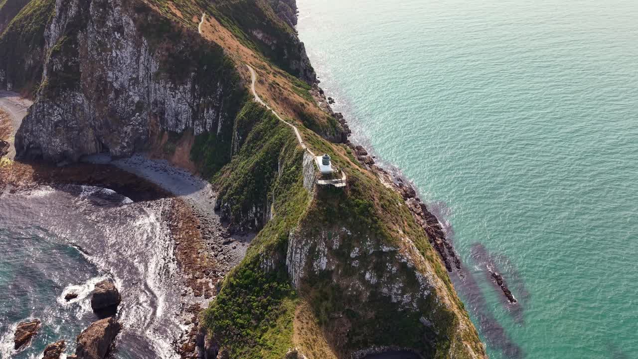360 drone orbit around Nugget Point lighthouse showing wild beach, waves and calm ocean at sunset