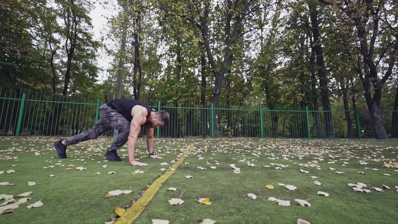 Powerful man doing push-ups in action at sport ground. Handsome athlete with muscular body during his workout outdoors. Slow motion.