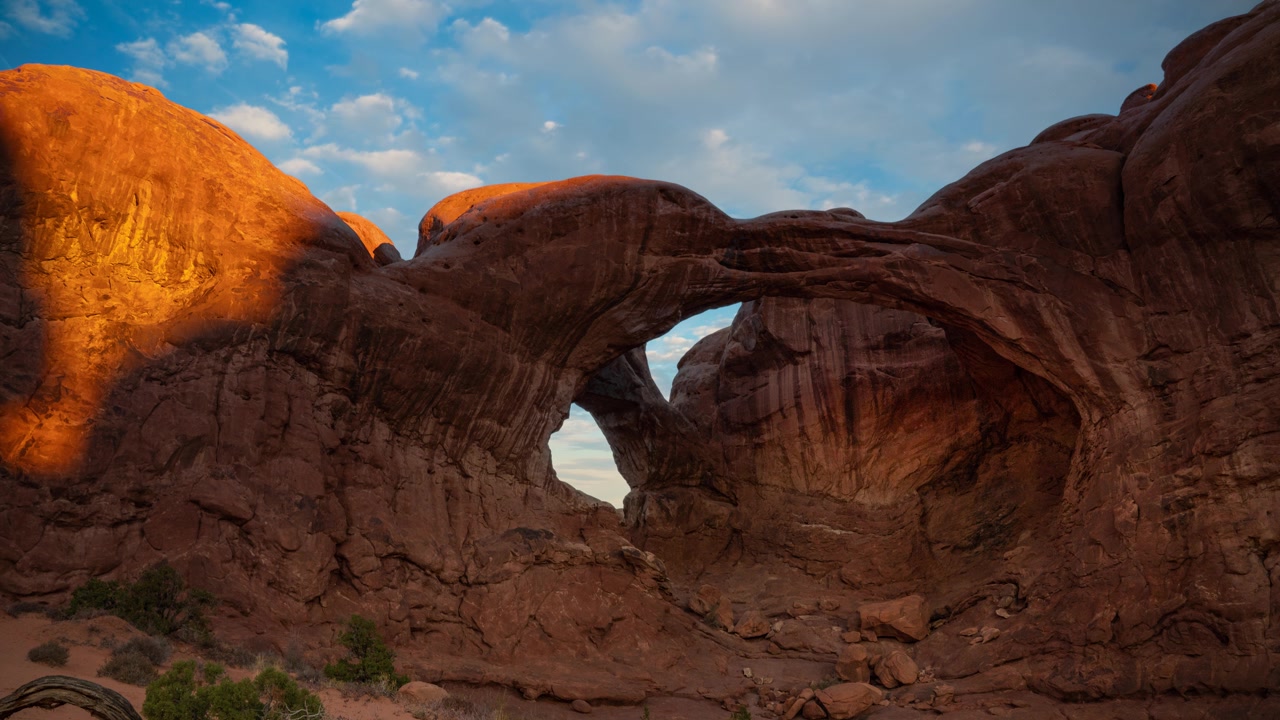 Rekaman selang waktu awan bergerak melintasi langit biru di atas Double Arch di Taman Nasional Arches, Utah, AS