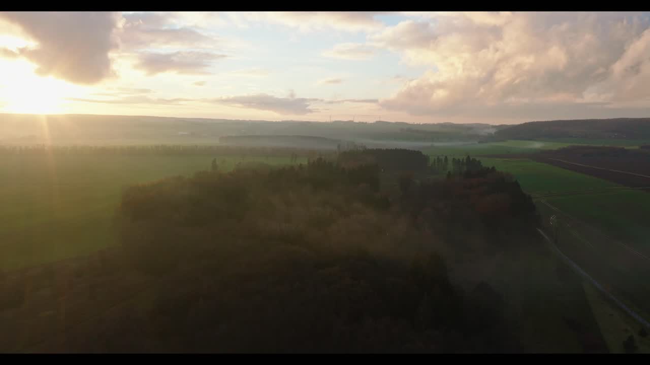 toma aérea de drones hacia adelante que muestra pequeñas colinas cubiertas de densa vegetación verde con cielo nublado a lo largo del campo rural