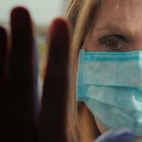 a woman in a mask comes into contact with her hand with her other hand through the glass