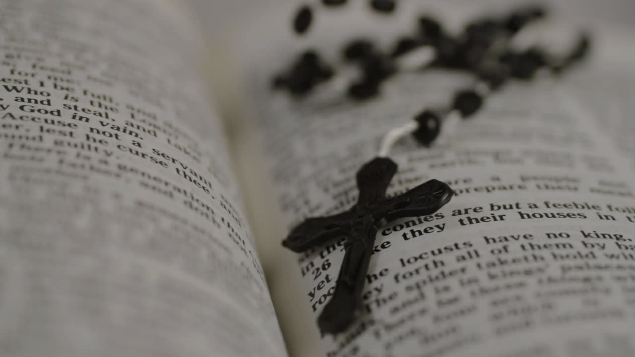 열린 성경에 놓인 묵주 구슬이 패닝 샷을 닫습니다.