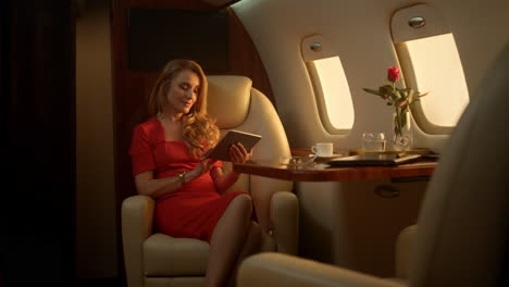 una mujer de negocios sonriente disfrutando de una tableta en un lujoso jet privado a la luz del sol.