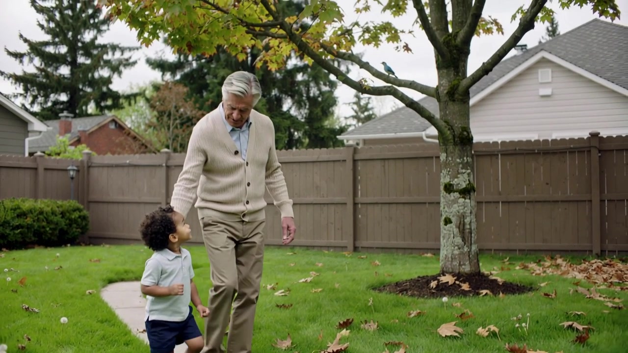 Walking cardigan-clad senior guiding polo-clad child stepping onto backyard path, pointing at tree