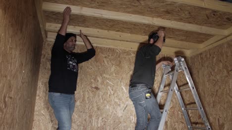 two workers installing a wooden ceiling panel on a framed structure.