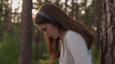 mujer triste con auriculares en el bosque. mujer joven parece molesta escuchando música pensando en la soledad durante el paseo al atardecer. reflejos en el aire fresco